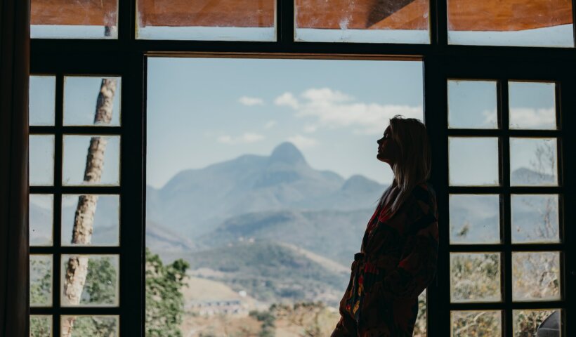 woman in red and black plaid dress shirt standing on window looking at mountains during daytime